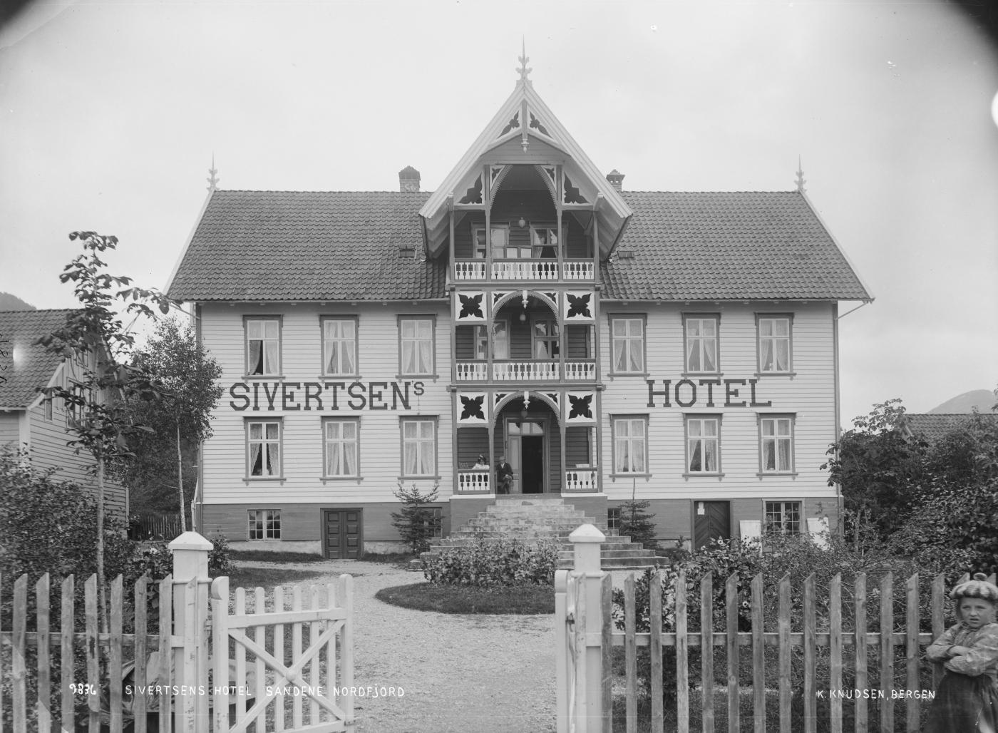 bilde i svart kvitt av eldre trebygning, tekst på huset er Sivertsens hotel