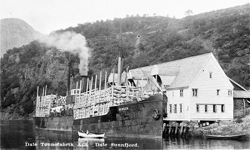 Skip foran stort trebygg, svart-kvitt