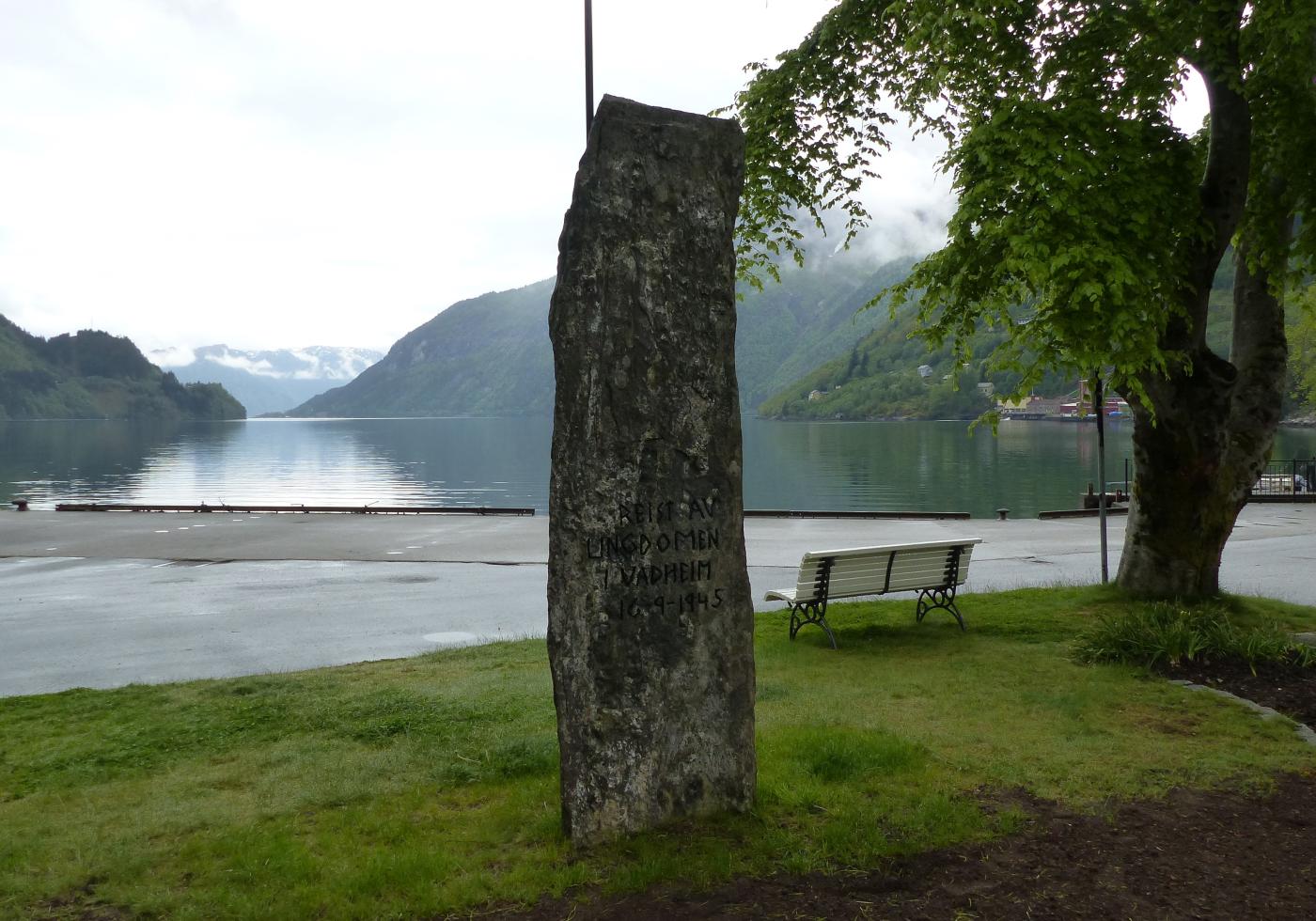 Minnesteinen i Vadheim over to falne i andre verdskrigen står i sentrum ved kaia og buss-stoppestaden. Framsida vender mot fjorden.