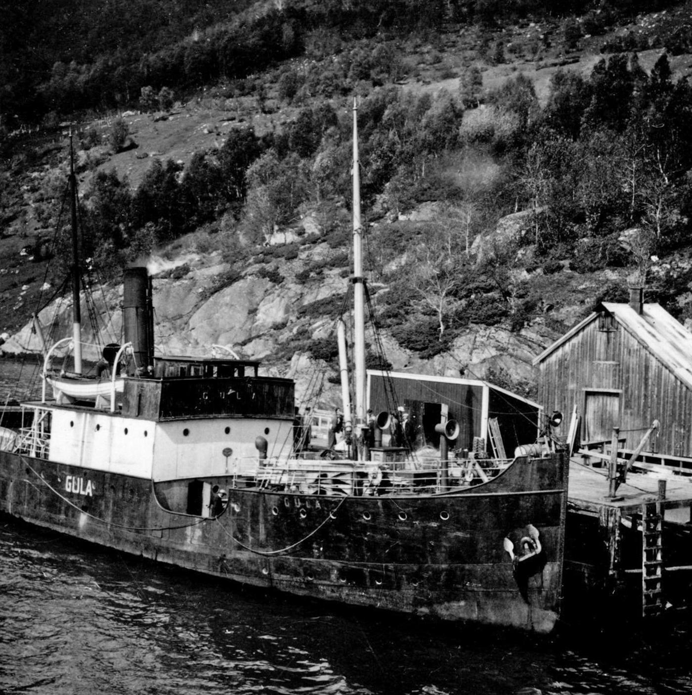 DS «Gula» til kai ved Holand i Holandsfjorden, Meløy kommune. Originalfotografiet finst i fotosamling etter Egil Furuhatt. Under krigen 1940-1945 var familien Egil Furuhatt evakuert frå Bodø til Holandsfjorden, Meløy kommune. Furuhatt fotograferte, og det er mykje truleg Egil Furuhatt som har teke biletet.