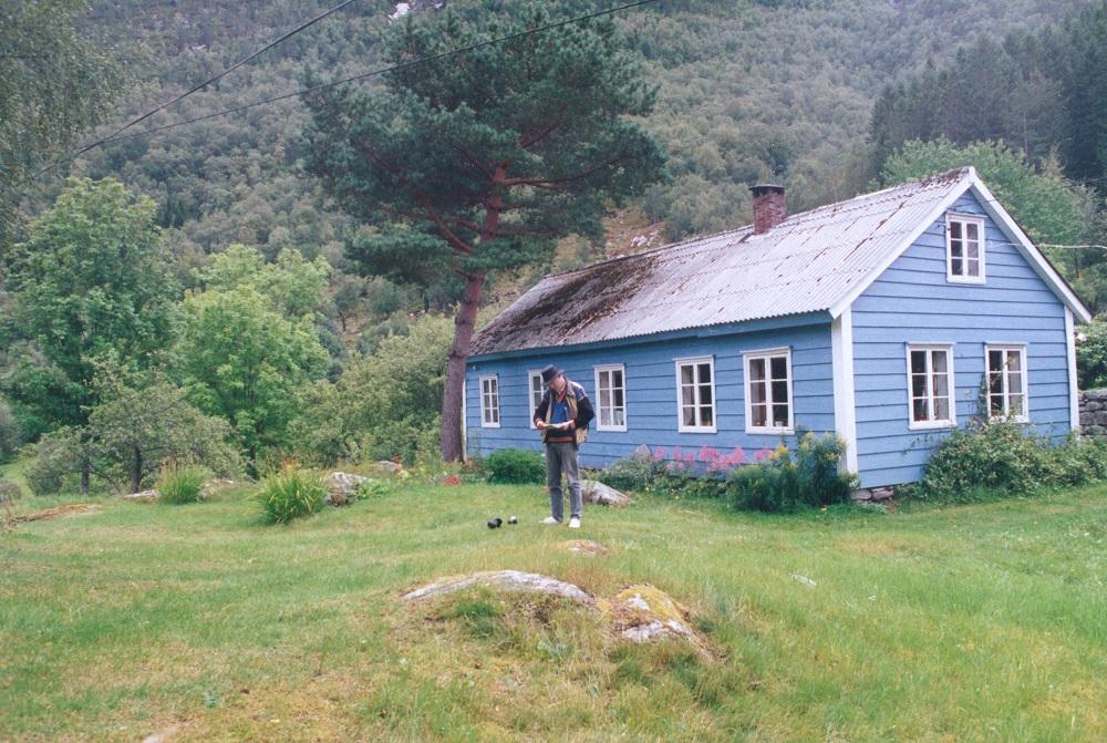 Stova på Sande der diktaren vart fødd. I framgrunnen ser vi kunstnaren Geir Hjetland som har laga minnestøtta over Sande.
