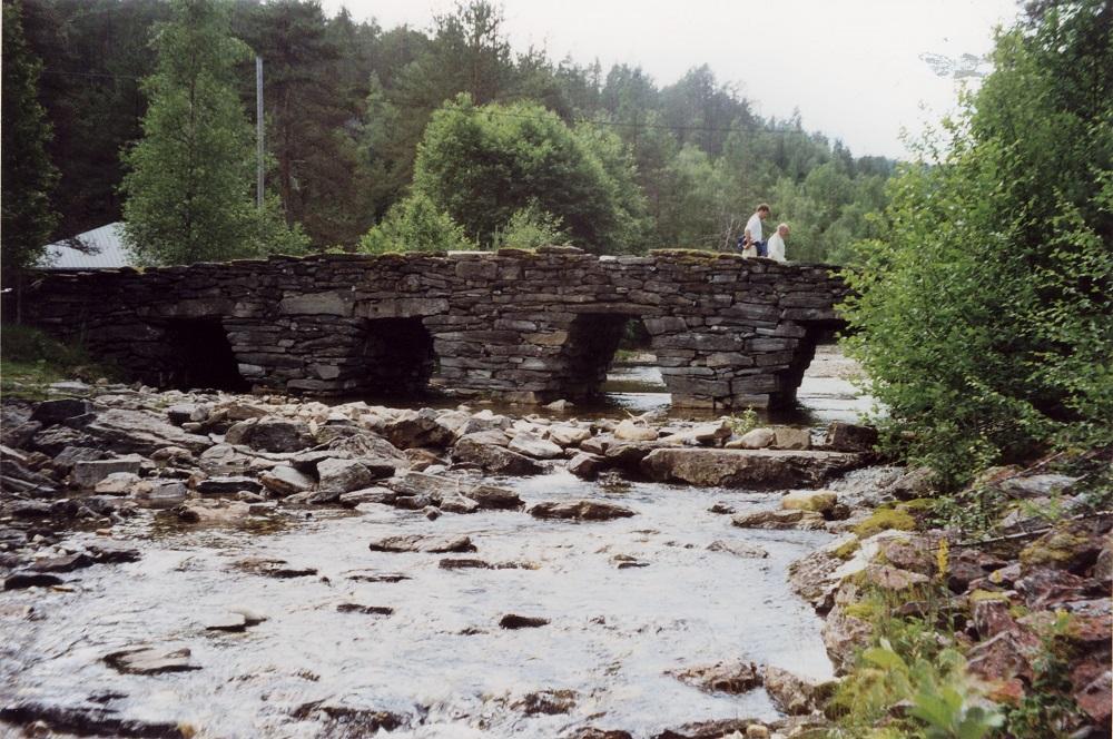 Steinhellebruene i Sindre/Øyane, Kvithellebrua, Storelvbrua og Nordelvbrua, var alle bygde i 1790-åra. Dei gamle bruene står att som minne om andre tider og andre byggjemåter. Kvithellebrua, som vi ser her, er nær 24 meter lang. Alle bruene har fundamente med trestokkar av osp eller furu, som enno ligg solide i fuktig elvebotn. 