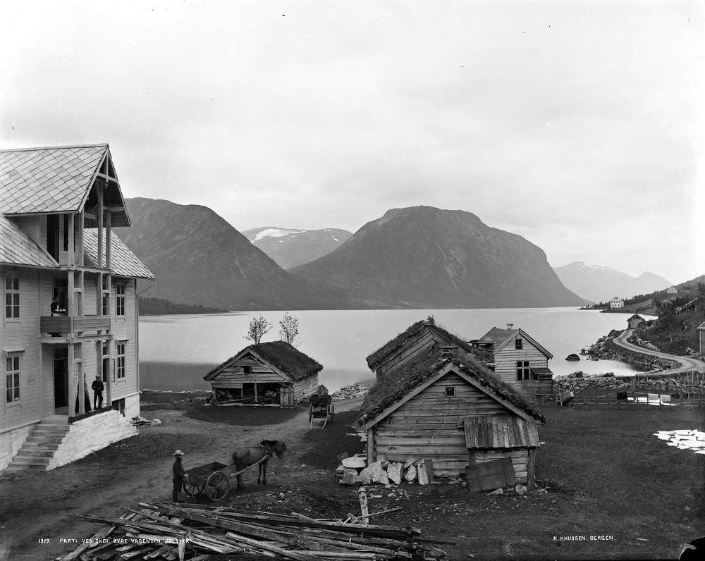 Nordenden av Jølstravatnet med det gamle Skei Hotel til venstre og postvegen til høgre. Til venstre ser me litt av hotellet Tollef Gabriel Skrede opna i 1889. Hotellet fekk konkurranse av av Stanley Hotel som vart bygd 1 km lenger sør. Skrede kjøpte hotellet då det gjekk gjekk konkurs i 1894, og flytta det opp til Skei.

 