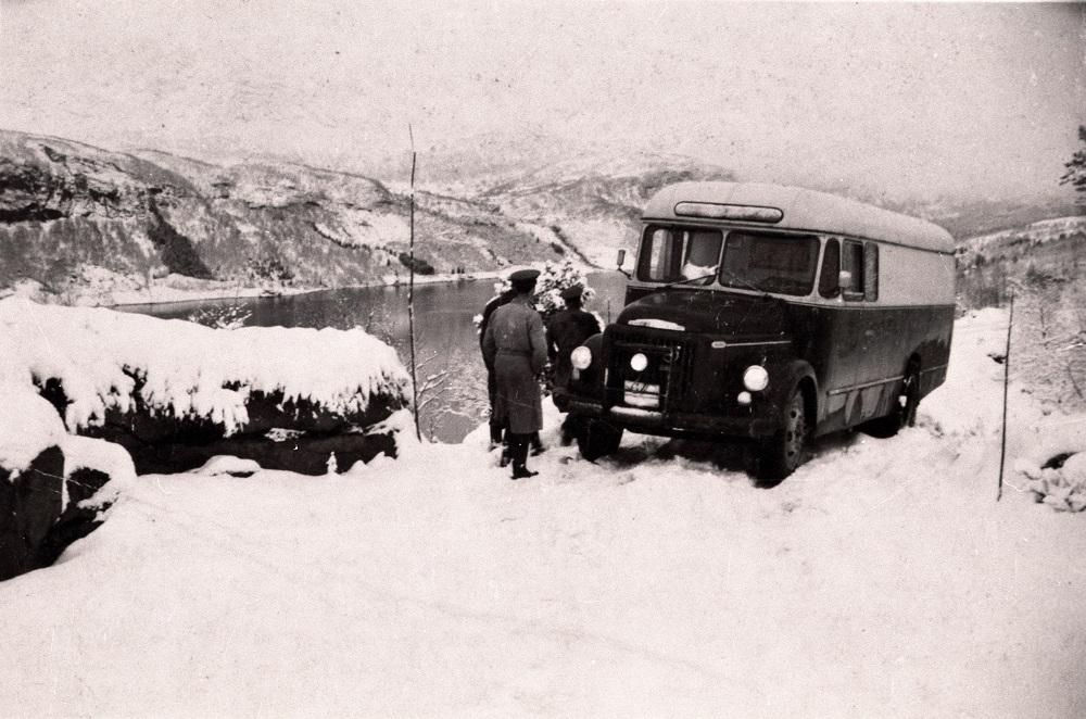 Bilar, lasteruter- og personruter vart etter kvart ein viktig del av kommunikasjonen i fylket, og synet på vegtrafikken tok så smått til å endra seg. På 1930-talet vart stamvegruter prioriterte. Gaularfjellsvegen og Rørvikfjellet vart ein del av riksvegsambandet (rv. 13) frå Kaupanger til Florø. Men det var så ymse med brøytinga over fjellet. Her ser vi ein Volvo 1955-modell som må leggja på kjettingar. Vi ser Haukedalsvatnet i bakgrunnen.

 