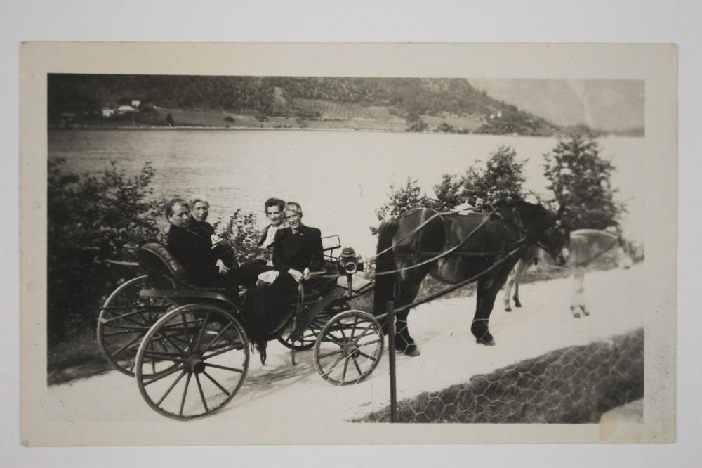 Då vegen var ferdig frå Holmen (Balestrand sentrum) til Ese i 1895, var det stor fest. Bygdepoet, kyrkjesongar og klokkar A. P. Øvrebø dikta ei vise til festen, der eitt av versa går slik: 

"Og skranglekjerrer og skjeive meier/ 
Og fillegampar og vidjegreier/
Det kverv nok burt etter denne dag./ 
Jau, eg skal sei her vert anna slag."

Og som vi ser er i alle fall køyredoningen ganske fine. Hest og karjol er på veg til Holmen. Damene bak i vogna er Marie Tuftedal og Brita Sundal. Framme sit T...