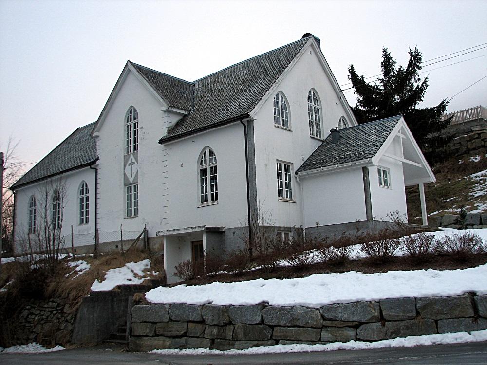 Samlingsheimen på Stårheim. Huset ligg tett attmed kyrkja på vestsida av elva. 