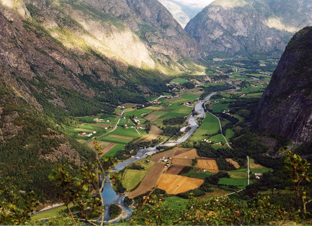 Utsikt oppover Lærdal frå Lunde mot Mo. Fylkesveg 272 går på sørsida av Lærdalselva (t.h.), E 39 på nordsida (t.v.). Vegen er ikkje utbetra til stamvegstandard. Planlegging av ny veg er svært vanskeleg i dette jordbrukslandskapet. Ein stamvegtrasé midt gjennom dalen vil gi store ulemper. Planleggjinga og byggjinga av stamvegen både gjennom Lærdal og vidare austover går svært seint, og det er ikkje politisk vilje til å auka tempoet. 

 