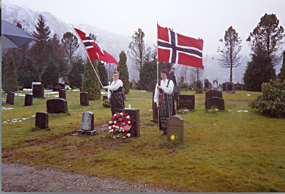 Frå markeringa ved grava til Olav Hjelle i 1990, 50 år etter det tyske åtaket på Norge og 50 år etter at Olav Hjelle fall under felttoget i Valdres. Grava til Hjelle på Stokkenes gravstad på Nordfjordeid, er den einaste krigsgrava i Eid kommune. Kvinnene med flagg ved grava er Wenche Noste (t.v.) og Ragnhild Bjørlo.
