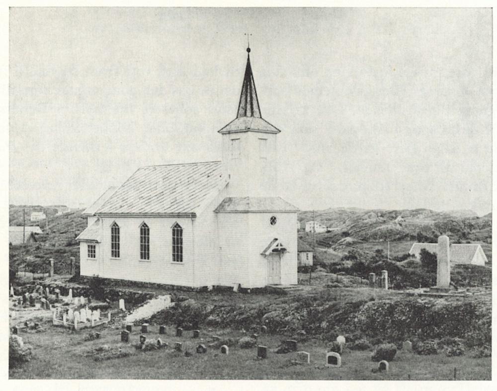 På Husøy står minnestøtta på høgd på framsida av kyrkja. Framsida vender mot vegen inn til kyrkja.
