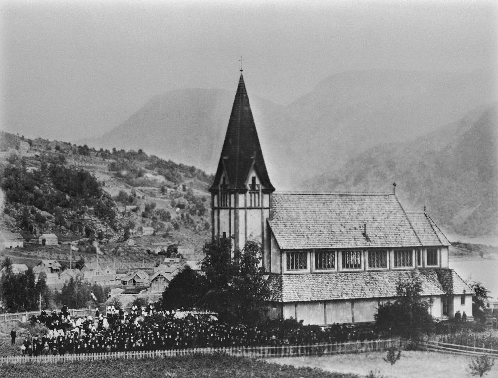 Bilde av kyrkje, fjell i bakgrunnen. Folkemengd. 