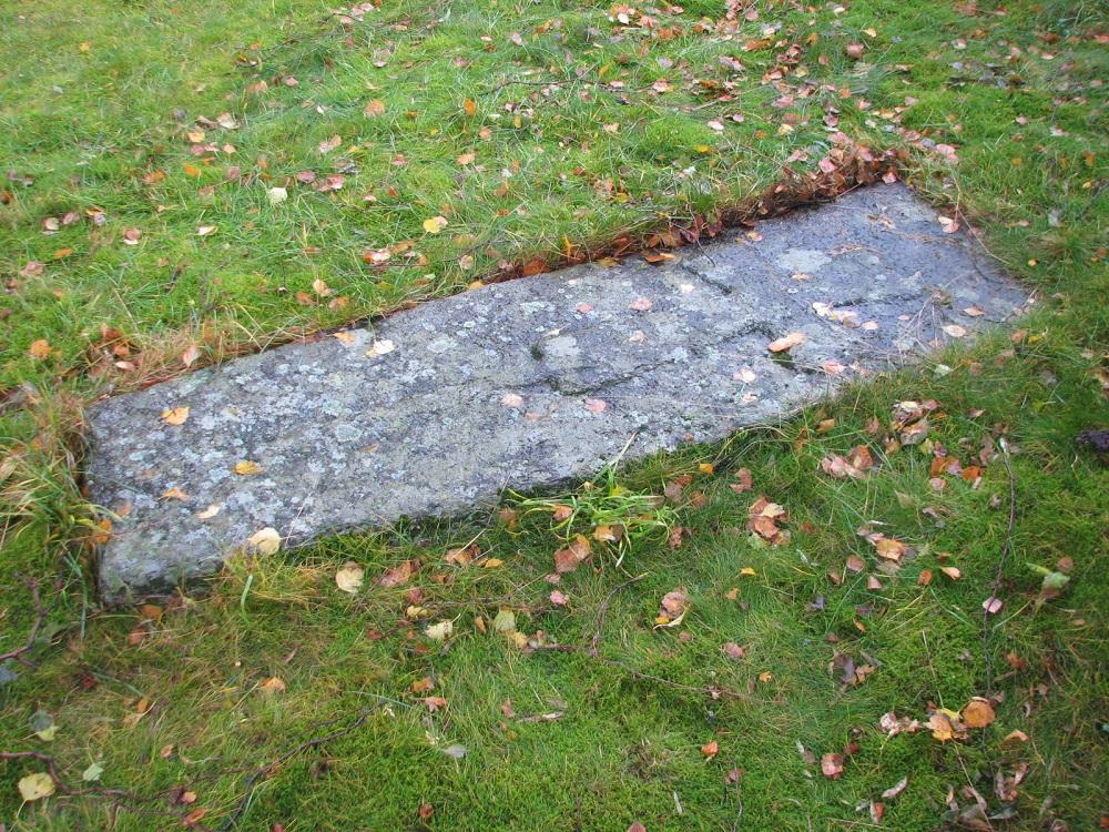 Mellomaldergravminnet ved Ortnevik kyrkje 2006. Steinen ligg heilt plant med bakken, og det er teikn til overgroing.

