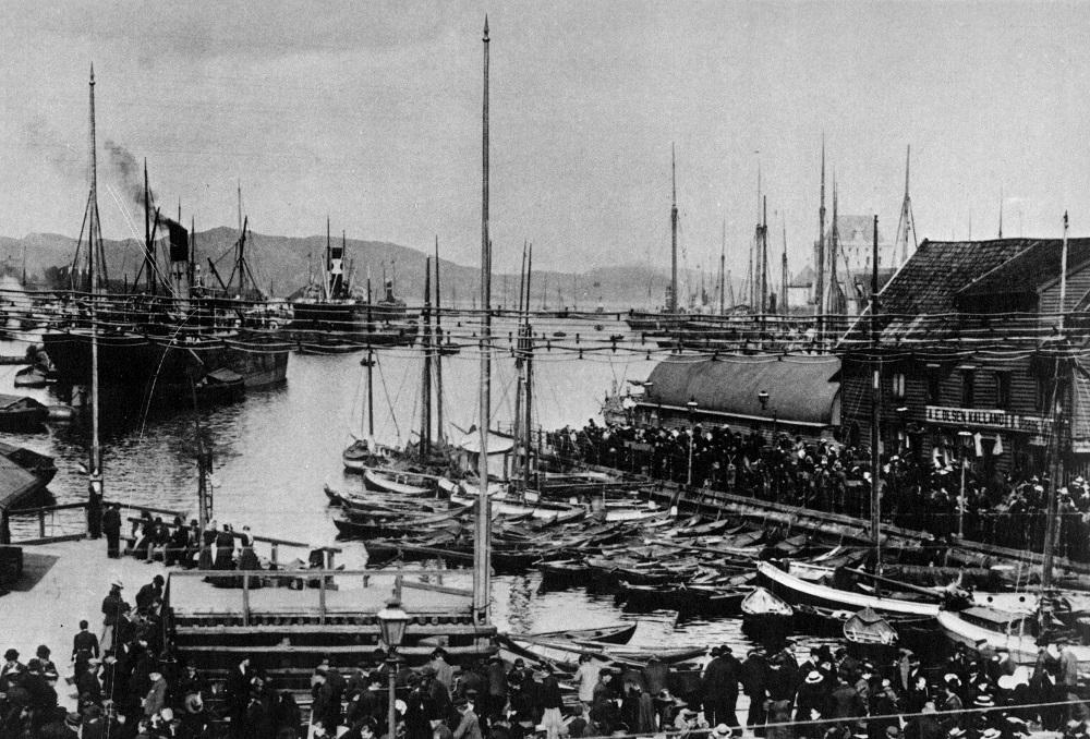 Biletutsnittet frå Bergen hamn i 1902 viser ei mengd ulike føringsbåtar som er i byen og vender varer, heile spekteret frå færingar, store-båtar, jakter og jekter. Fleire bomsegljakter ligg med akterenden inn mot kaikanten.<br />
I framgrunnen til venstre ser me den trekanta bryggja Triangelen. Det var stasbryggja der kongelege steig i land. Manglande kaiar gjorde at store damparar ligg langt inne på Vågen og vert lossa  eller lasta av føringsbåtar. På Zachariasbryggen er stor tilstrøyming kring dei...