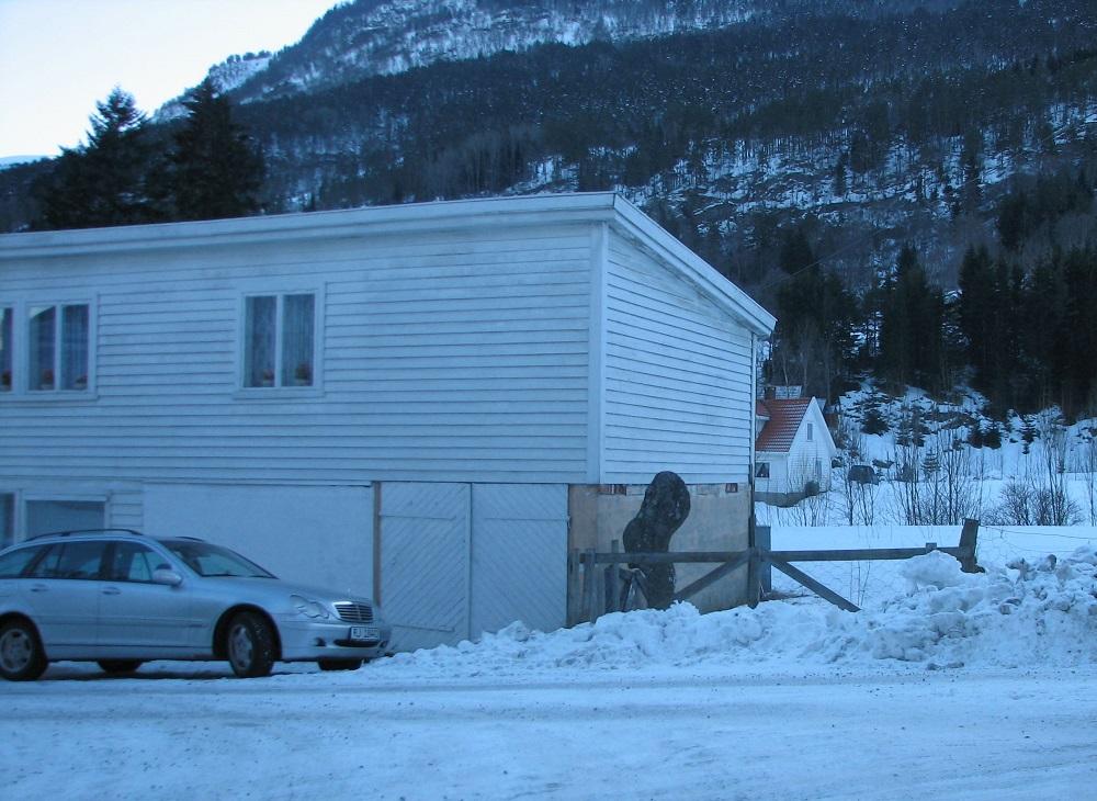 Steinen med namnet Kjøtbogen står tett attmed hjørnet av eit hus der vegen kjem ned til husa langs stranda i Solvorn.




