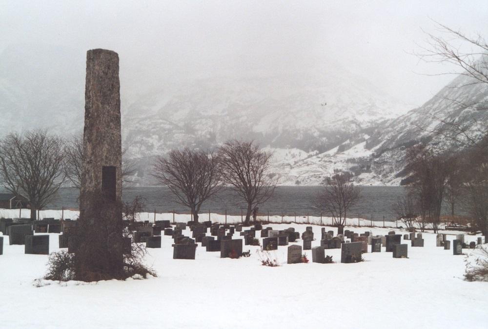 Den kring fire meter høge minnesteinen over falne i krigen 1940-1945 står på sørsida av kyrkja på Fosnes. I bakgrunnen ser me Oppstrynvatnet og Flogrenda.
