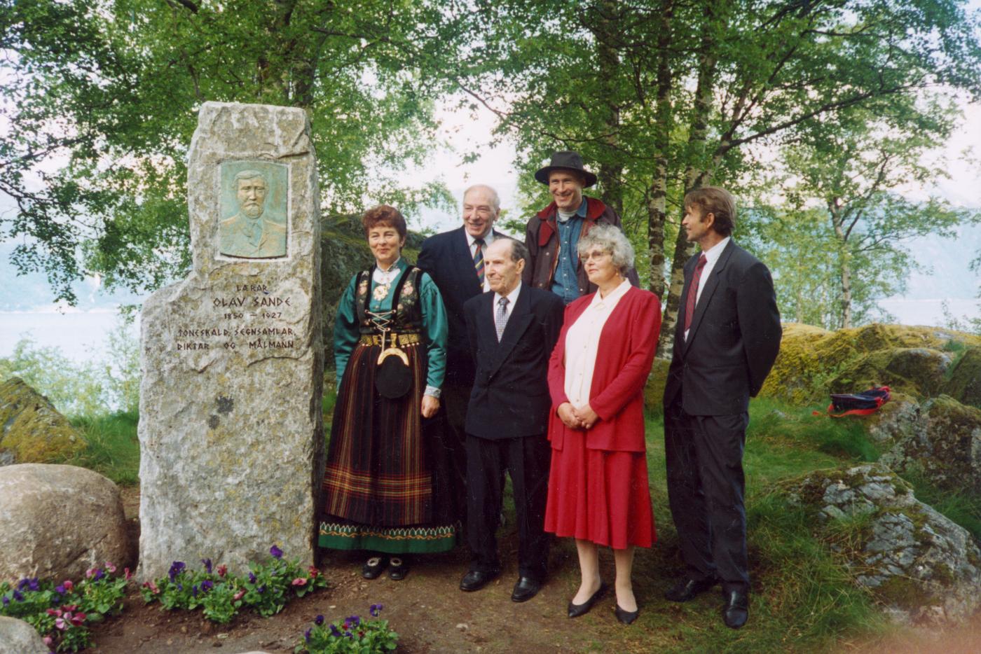 Frå avdukingshøgtida 4. juni 1994. Emnet til steinen fann dei i Taklegrenda i Brekke. Høyangerkunstnaren Geir Hjetland laga relieffet. Frå venstre: Ordførar Liv Lønne, Sverre Erdal (kultursjef), Geir Hjetland (kunstnar), Trygve Heggenes, Ruth og Harald Sande (eigarane av Sandegarden).