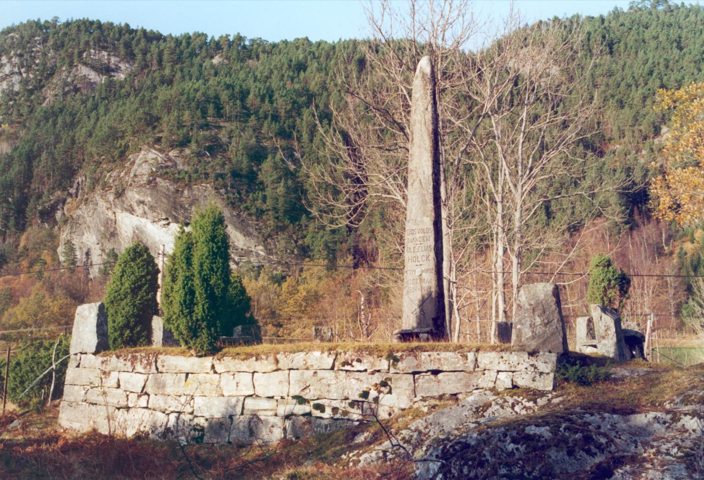 Minnebautaen over Eidsvoll-mannen Ole Elias Holck er reist på ei høgd like ved gardstunet i Alværa. Han er fundamentert i berget og ruvar kring 5 meter i været. På den oppmura foten rundt, er sett steinar i kvart hjørne. Hovudinnskrifta er på på den sørvende sida mot fjorden.