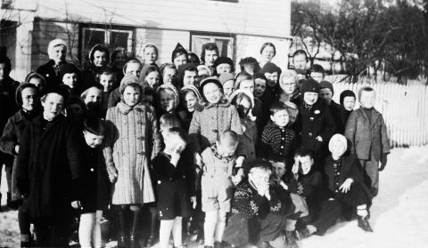 Søndagsskulen i Leikanger, ca 1940, fotografert framføre Sogns Barneheim, i Strandavegen. Dei vaksne bak i høgre hjørne, frå venstre, er truleg søndagsskulelærar Hansine Moen og styrar på barneheimen Unni Henjum.