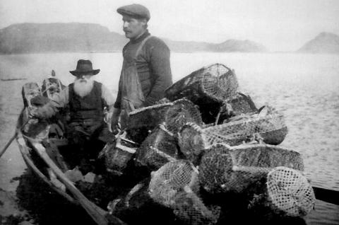 Setting av krabbeteiner. To karar i robåt med krabbeteiner, ved Nigardsøyna i Bremanger. Mannen ved årene er Mikal Kornelius Pedersen Nigardsøy. Den yngre mannen som står i båten er ein av dei fire sønene hans, Albert Bernt Mikalson Nigardsøy. Bak i båten ser vi hummerteiner. Dei var truleg på veg ut for å sette teinene.