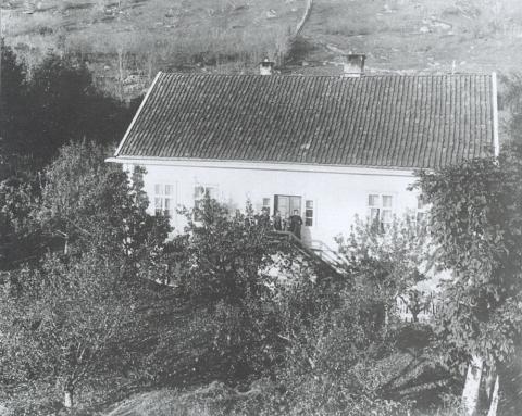 Klokkarbustaden kring 1900. På trappa ser me lærar og kyrkjesongar Hans Flesche med nokre av huslyden hans. Ein reproduksjon av originalfotografiet heng i kyrkjelydshuset Klokkargarden.
