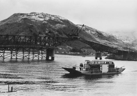 Her ser vi gammal og ny tid i Sogndal. I bakgrunnen er ein i ferd med å byggja Loftesnesbrua som vart opna i 1958. I framgrunnen går ferja som vart nytta til å frakta bilane over sundet. Ferjeførar var Bernt Pedersen og Kristian Fardal.   

