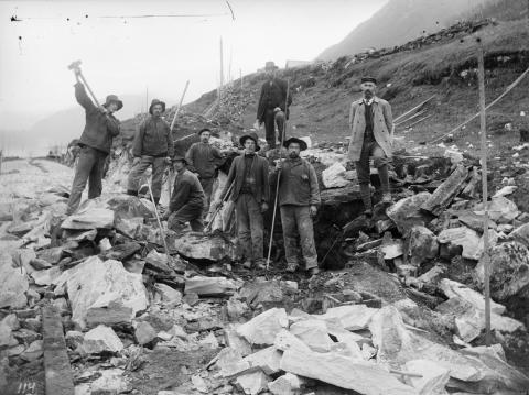 Vegarbeid ved Rognes langs Hornindalsvatnet, truleg i 1909. Frå venstre: Anders Vikøren, Rasmus Hole, Ukjend, Johan A.Nesbakk, Ukjend, Matias Nord, og oppsynsmann Bruland frå Sundfjord. I hatt og frakk til høgre står overingeniør Knud Knudsen, seinare vegsjef i fylket. 

 