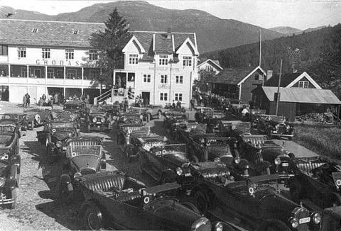 I 1922 vart vegen langs Strynevatnet ferdig, og det vart samanhengande veg på strekninga Hornindal-Stryn-Geiranger. "Overlandkøyringa" tok seg opp. Ruta var i regelen Øie (Norangsfjorden)-Grodås-Stryn-Strynefjellet-Geiranger. Konkurransen om køyringa var stor, med fem ulike selskap som fordelte køyringa mellom seg. Køyringa vart utført med personbilar fram til 1973, då bussane overtok. Biletet er teke sommaren 1936. På Raftevolds Hotel fekk dei kaffi og kaker, og etterpå fotograferte turistane Europ...