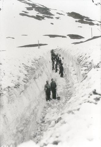 Her ser vi eit parti av Strynefjellsvegen blir brøytt for hand, og korleis dei spar seg lagvis gjennom snøen. Vi ser vi og tydelege spor etter moldinga (mylding). 

 