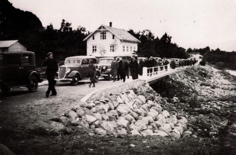 Frå vegopninga i 1937. Vi ser bilkortesjen på brua over Njøsaelva. Brua vart ferdig i 1935, og før den tid gjekk det ei bru på skrå over elva om lag 20 m lenger oppe. Det kvite huset i bakgrunnen står der Fylkeshuset står no. 