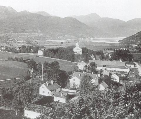 Oversynsbilete over Skei kring 1895. Nærmast ser vi dei to tuna på Indre Skei, sorenskrivargarden Volden, bnr. 24, og utanfor bnr. 25 på Indre Skei. Den gamle kontorbygningen ligg på tunet til venstre. Her på Tåene ligg bygningar på rekkje og rad som minner om det gamle embetsmiljøet på Skei: Volden, Indre Skei, og Kapteinsgarden Ytre Skei ved kyrkja. Den gamle prestegarden ligg utanfor biletkanten til venstre.
