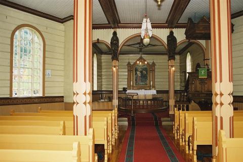 Frå interiøret i kyrkja, skipet sett mot koret. Både i skipet og koret er der boga vindauga med småruta glas. Taket i skipet er delt inn i kvite felt, og delt opp av raudmåla bjelkar med gulldekor. Også i koret er taket inndelt i felt, men desse har ein enklare dekor.