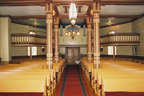 Frå interiøret i kyrkja, skipet sett mot galleriet og våpenhuset. Fargane er mykje lik dei opphavlege. Veggene er gule, i skipet har dei brystning. Benkene, som sist vart pussa opp i 1994, er brunmåla. I taket heng eit votivskip. Orgelet frå 1914 har åtte stemmer, og er bygt av Olsen og Jørgensen.