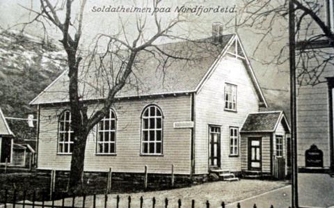 "Soldatheimen paa Nordfjordeid" står det trykt på dette postkortet frå kring 1910. Dei første åra vart bedehuset nytta som velferdshus for soldatane når det var militærøving på eksersisplassen på Nordfjordeid.