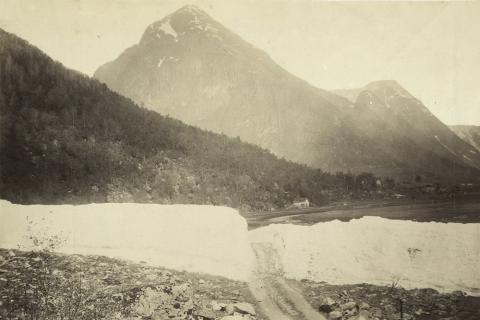 Mundalsskreda på vestsida i Fjærland fører årvisst enorme snømengder ned mot fjordbotnen, og det kan gå langt utpå våren før rassnøen er borte. Her ser vi at vegen er opna gjennom rasområdet. Vegan vart seinare omlagd med trase nærare sjøen for å unngå skredfaren.