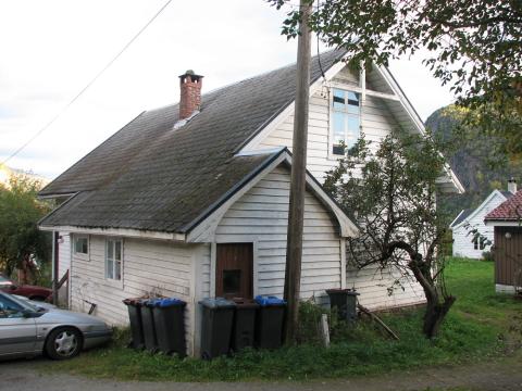 Bedehuset sett frå søraust. Eit frukttre, ein telefonstolpe, bosspann og parkerte bilar har fått lov å koma heilt inn til husveggene.



