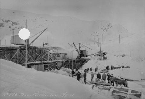 Grimsosen februar 1917. Arbeidet med dammen er påbegynt, og eit overbygg held snøen vekke frå sjølve damstaden. Hest og slede vart nytta vinterstid for å få fram forsyningar til anleggsdrifta. Med tida vart det bygd taubanestasjon, verkstadbrakke, toalett og messe for arbeidarane på Grimsosen.



