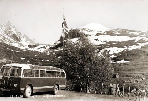 Utsyn frå Turtagrø Hotell mot sør, Dyrhaug (th) og Skagastølstindane med Storen (Store Skagastøstind) (tv). Sogn Billag sin buss med registreringsnummer S-150 står på parkeringsplassen. 