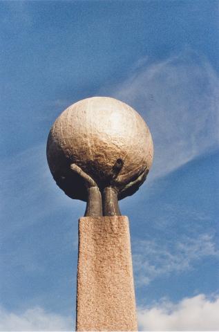 Den seks meter høge granittsøyla dannar fundamentet for to sterke hender som held oppe ei gullforgylt kule, støypt i bronse, og med diameter 1,36 m. Kula symboliserer jordkloden.