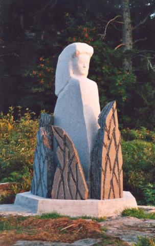 Steinstykka i mørk bergart rundt kvinnefiguren symboliserer elden, bålet.
