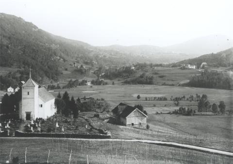 Bygstad kyrkje før ho vart flytta frå garden til Reita i 1939. Siste gravferda var i 1936, men alt i 1916 hadde gravplassen på Reita som vi ser i bakgrunnen til høgre, vorte vigsla og teken i bruk. 
