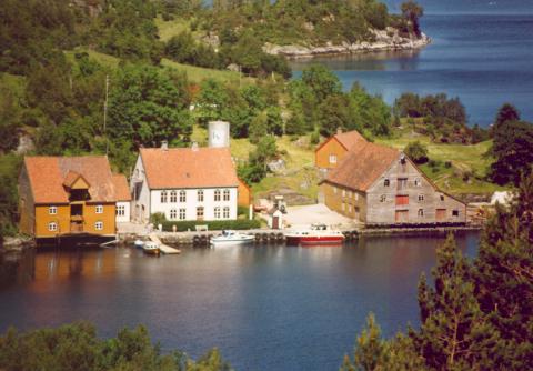 Rugsund var frå gamalt av ei mykje søkt jektehamn og gjestgjevarstad. Her ser me staden ein sommardag tidleg på 1990-talet. Klemt inne mellom det kvite våningshuset og sjøbua til venstre ligg butikken.