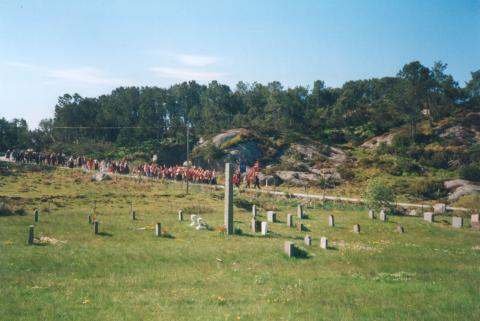 17.mai-toget på Mjømna 1999 på veg til kyrkja der det kvart år er markering ved minnesteinen på grava til Konrad Byrknes. Steinen er vel 3 meter høg, 55 cm brei og 23 cm tjukk.
